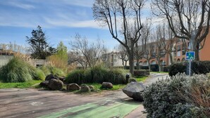 Zona residencial con calle pavimentada, carril bici verde, rocas grandes y arbustos.
