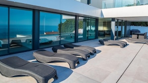 Et moderne udendørs loungeområde med flere fletstole og en glasindrammet terrasse med udsigt til havet.