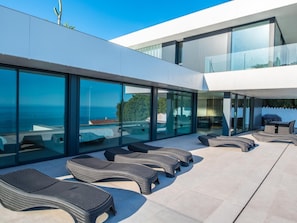 Ein moderner Außenbereich mit mehreren Korbsesseln und einer gläsernen Veranda mit Blick auf das Meer.