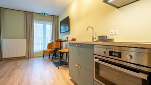 A modern kitchen with a built-in oven, a microwave, and a sink. There are two chairs and a table in the dining area. - Appart Hotel En Ville - Studio 2 persons in the center of Bastogne (Bastogne)