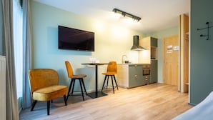 A modern kitchen with a flat-screen TV, wooden cabinets, and a dining area with two chairs. - Appart Hotel En Ville - Studio 2 persons in the center of Bastogne (Bastogne)