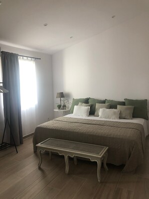 A bedroom with a bed, a bedside table with a lamp, a window with curtains, and a bench. - Stunning 'Finca Clos' with Mountain View, Private Pool, Garden, A/C & Wi-Fi (BORRASSA)