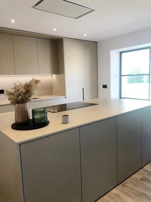 A modern kitchen with a large island, recessed ceiling lights, and a window providing natural light.