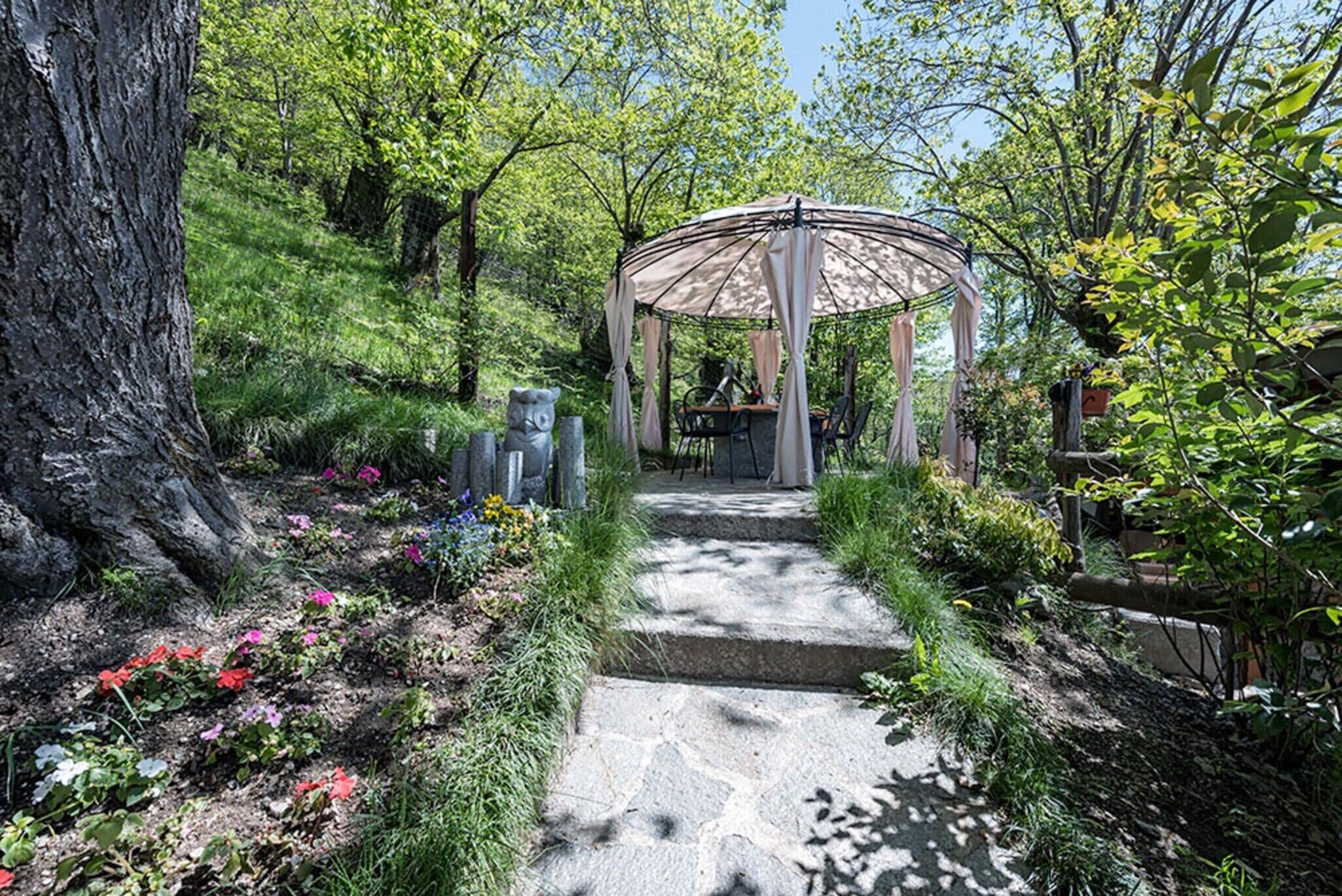 Ein Garten mit einem Gazebo, einem gepflasterten Weg und verschiedenen Pflanzen.