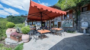 Une terrasse extérieure avec un sol en pierre, des tables, des chaises et un grand parasol rouge.