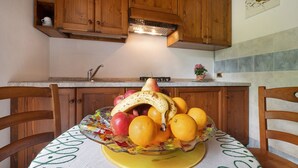 Une cuisine avec des meubles de rangement en bois, un panier de fruits sur la table et un pare-feu en carreaux.