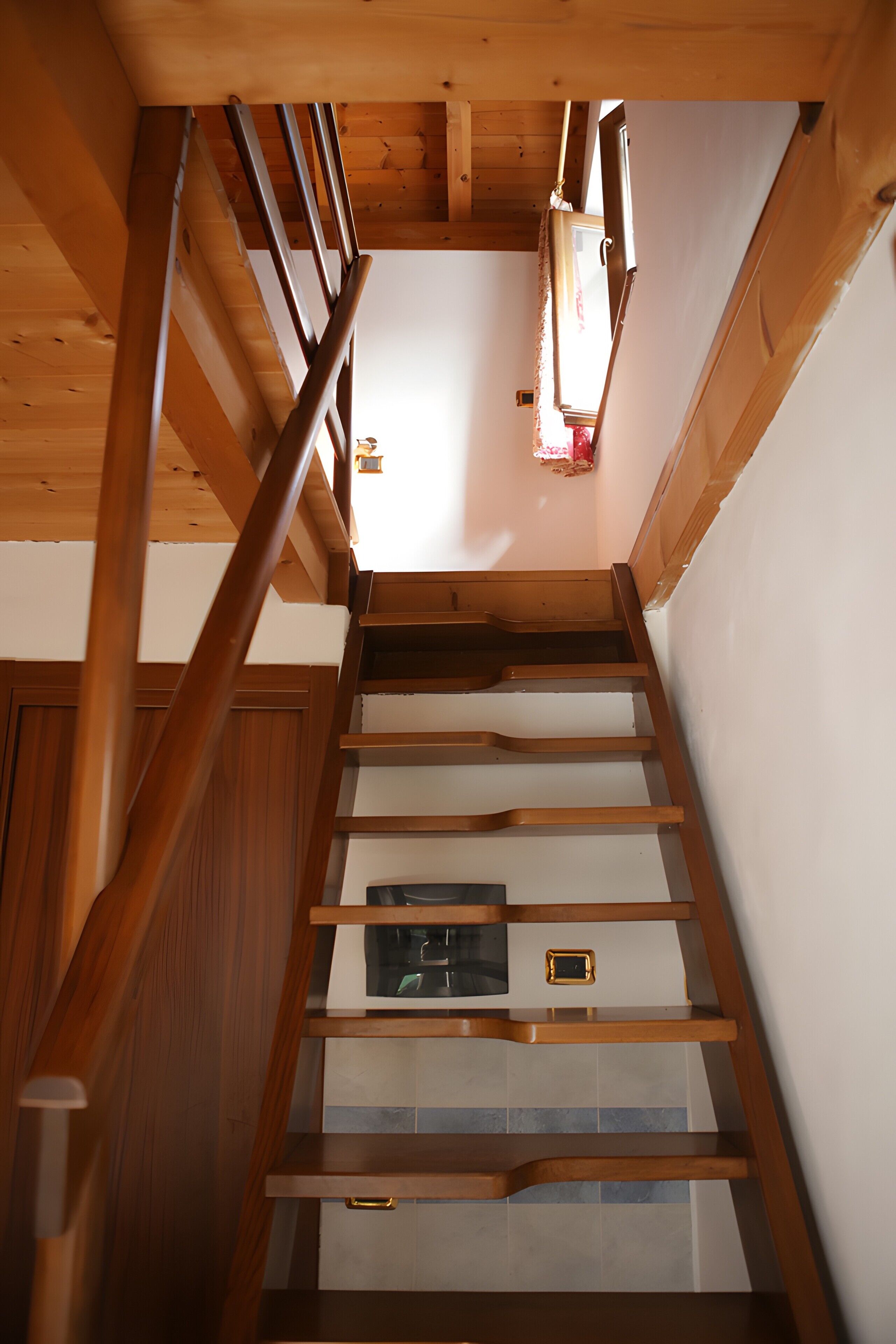 Un escalier en bois avec une rampe, une petite fenêtre et un luminaire.