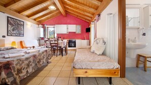 Una habitación acogedora con techo de madera, cama, mesa de comedor con sillas, zona de cocina y baño con lavamanos y espejo.