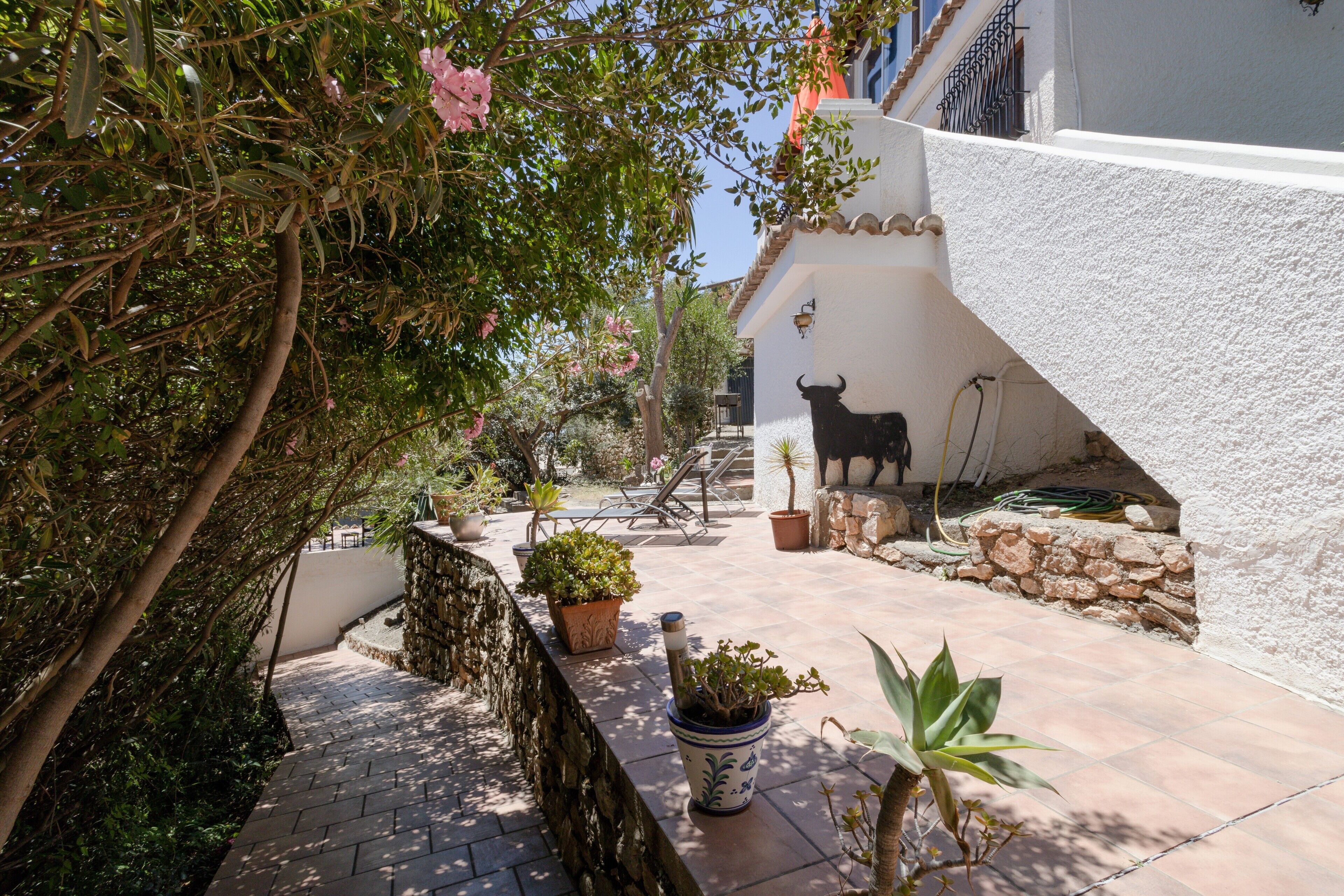 A courtyard with a stone wall, potted plants, a bull sculpture, and a tiled patio.