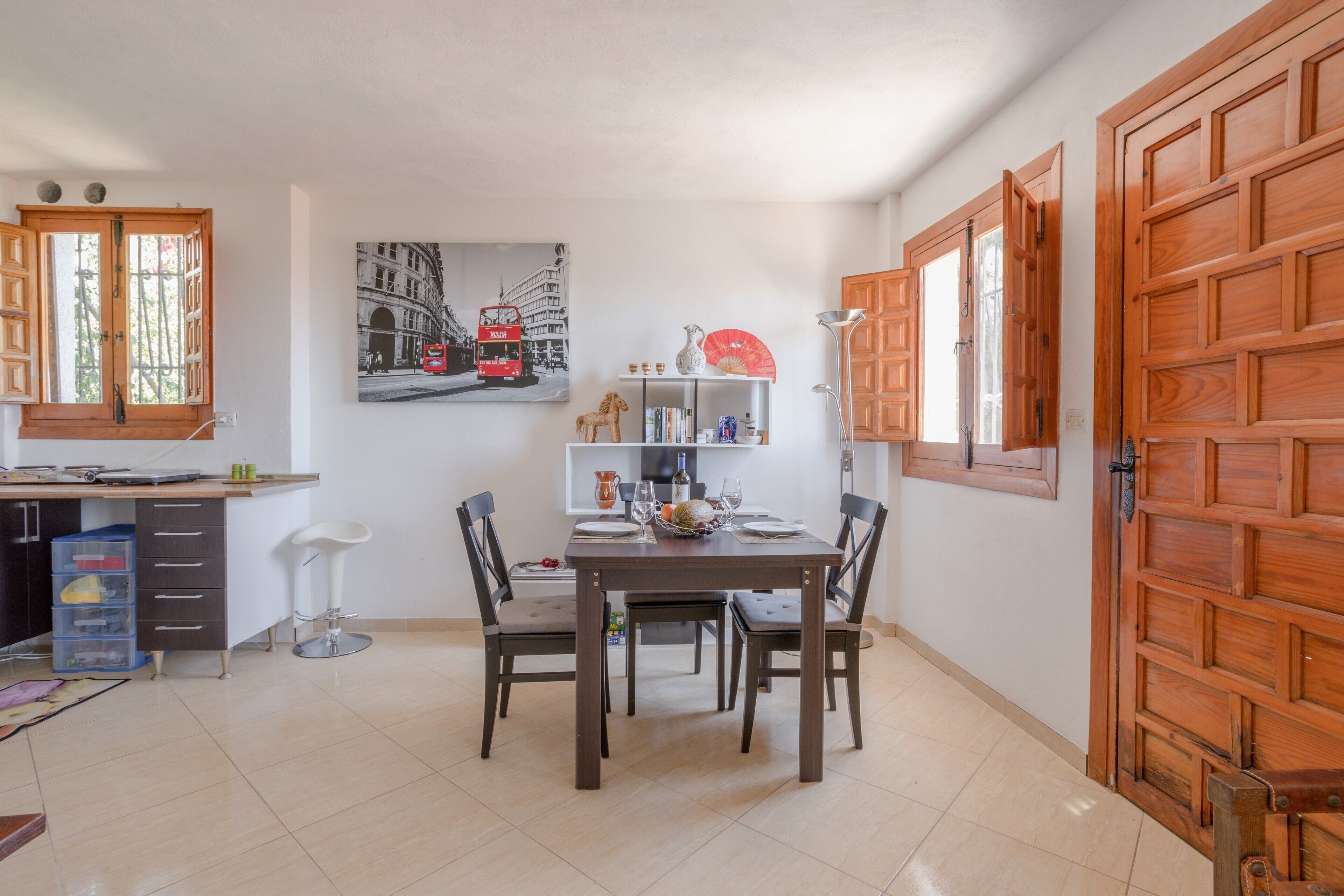 Un comedor con una mesa de madera, sillas y un cuadro de un autobús rojo de dos pisos.