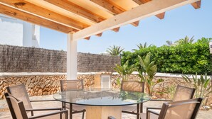 Un patio al aire libre con una mesa y sillas de vidrio, rodeado de muros de piedra y vegetación.