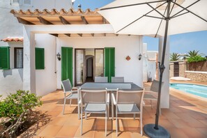 Eine Terrasse mit Tisch und Stühlen, ein Schwimmbad und ein Gebäude mit grünen Fensterläden.