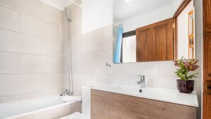 Une salle de bain avec une baignoire, des toilettes, un meuble-lavabo avec un miroir et une plante en pot.