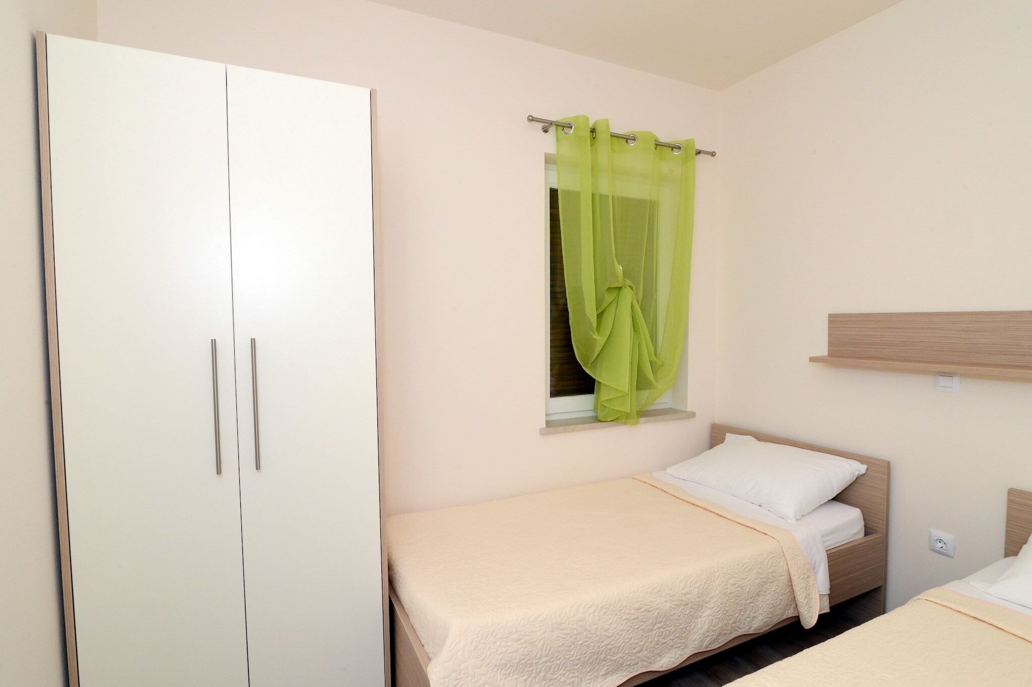 A bedroom with a single bed, a wardrobe, and a window with a green curtain.