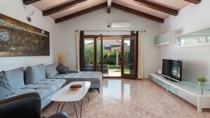 Una sala moderna con un sofá, una mesa de centro, un televisor y un ventanal corredero que da a un área exterior.