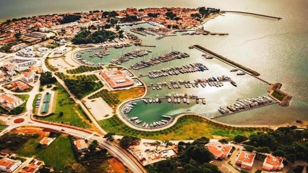 Vista aérea de un pueblo costero con un puerto deportivo, zonas residenciales y una glorieta.