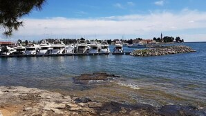 Una marina con barcos amarrados, una costa rocosa y un pueblo lejano con edificios y una torre.