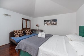 Une chambre d’hôtel avec un lit, un canapé, une petite table sur laquelle se trouve un vase, et un tableau représentant une vue sur la ville accroché au mur.