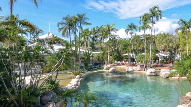 A resort with a pool surrounded by palm trees and lounge chairs.