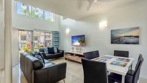 A spacious living area with a black leather sofa, a dining table with chairs, and a large window offering a view of the outdoors.