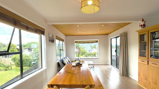 Un vaste espace dédié à la salle à manger, avec une longue table en bois, des bancs et un plafond haut orné de panneaux en bois.