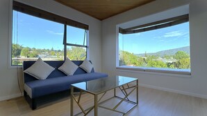 Un salon moderne avec un canapé bleu, une table basse en verre et de grandes fenêtres donnant sur un paysage verdoyant.