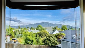 Une pièce dotée d’une grande fenêtre donnant sur un quartier résidentiel, avec des maisons, des arbres et des montagnes en toile de fond.