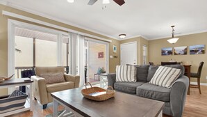 A spacious living room with a beige sofa, a gray sofa, and a wooden coffee table. There is a wicker basket on the table and a striped pillow on the gray sofa. - Tybeedaze at the Beach! | Heated Pool Access (Tybee Island)