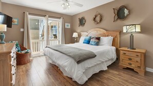 A bedroom with a bed, a nightstand, a dresser, a ceiling fan, and a view of the outside. - Tybeedaze at the Beach! | Heated Pool Access (Tybee Island)