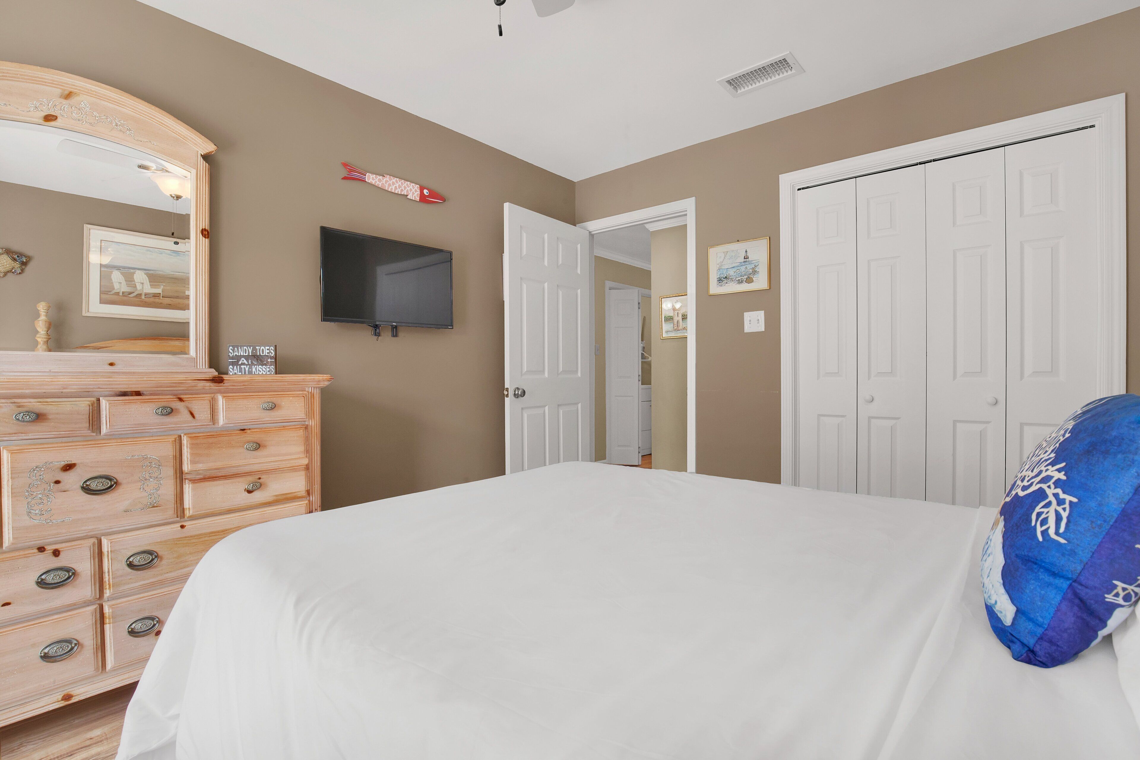 A bedroom with a bed, dresser, TV, and white doors.