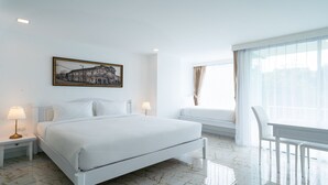 Une chambre d’hôtel avec un grand lit, des lampes de chevet, une fenêtre avec des rideaux et un tableau représentant un paysage urbain accroché au mur.