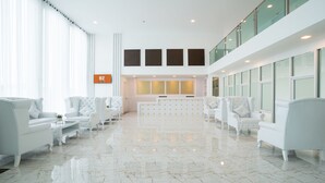 Un hall d’entrée spacieux, doté de canapés en cuir blanc, d’un comptoir de réception et de grandes fenêtres.