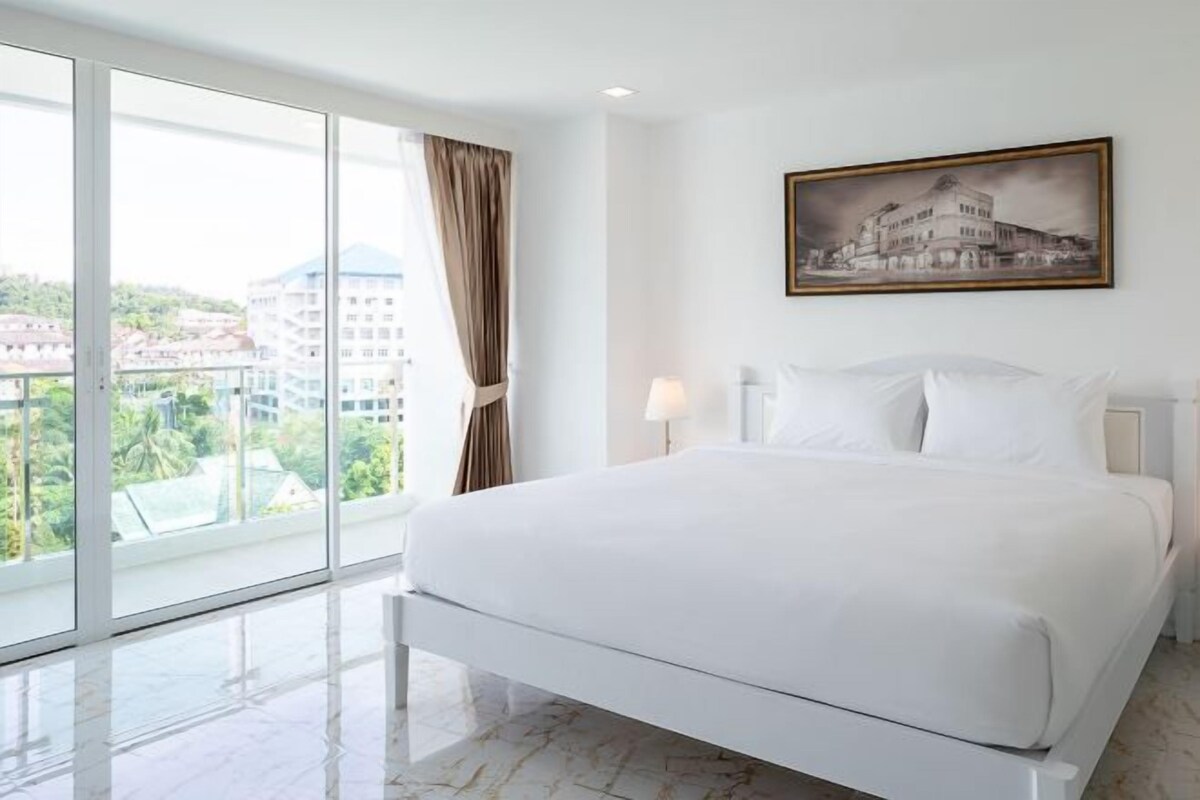 Un cuarto de hotel con una cama grande, una ventana que da a edificios y un cuadro en la pared.