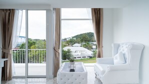 Une pièce spacieuse dotée d’une grande porte-fenêtre coulissante donnant sur un balcon, d’un fauteuil blanc à revêtement en tissu et d’une petite table d’appoint agrémentée d’une plante.