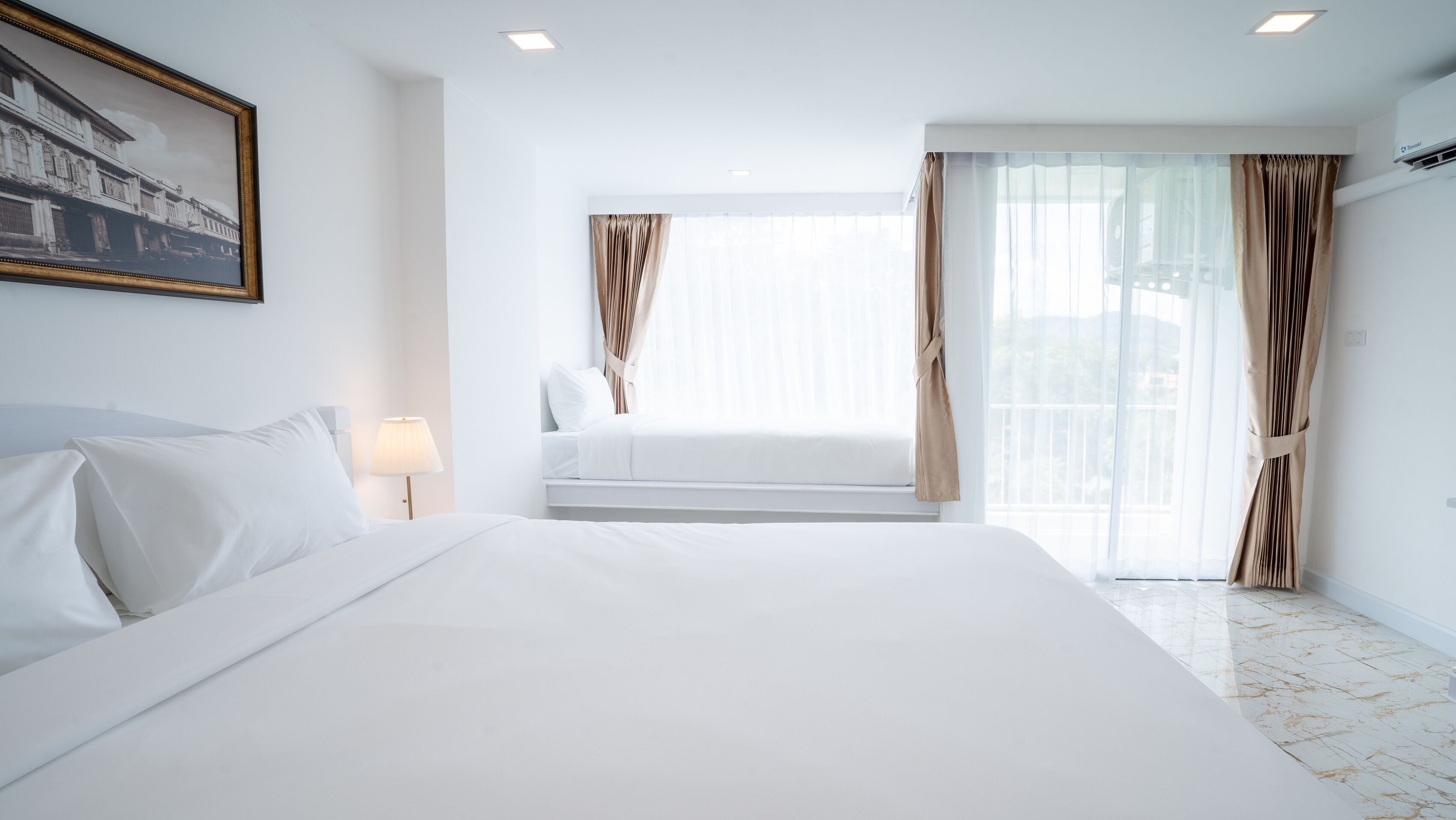 A hotel room with a large bed, a bedside table with a lamp, a window with curtains, and a view of the outdoors.