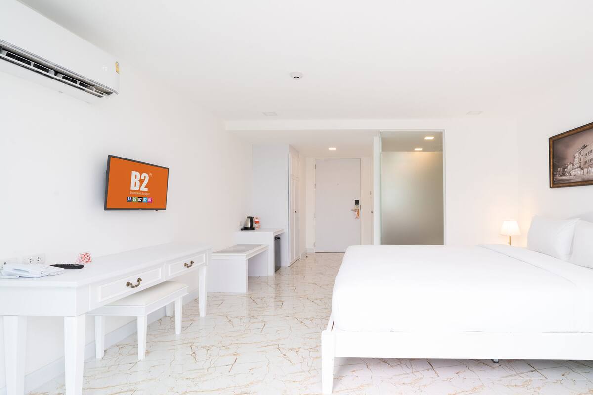 A hotel room with a bed, a desk, a television, and a painting on the wall.