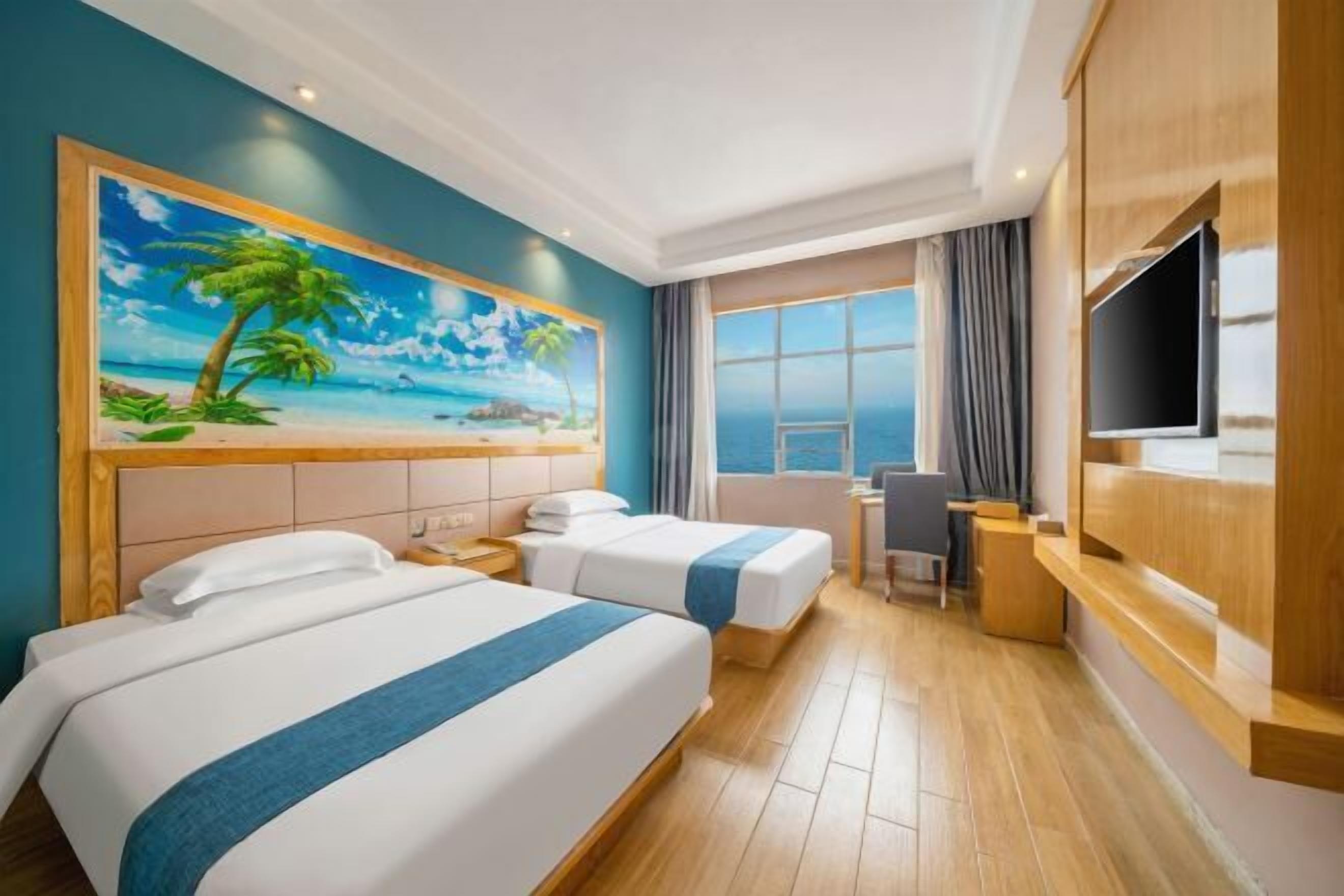 A hotel room with two beds, a desk, a chair, a TV, and a large window with a view of the sea.