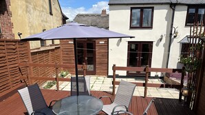 A patio with a round glass table and four chairs, surrounded by a wooden fence and a brick wall. - 2 Pound cottage (Gloucester)