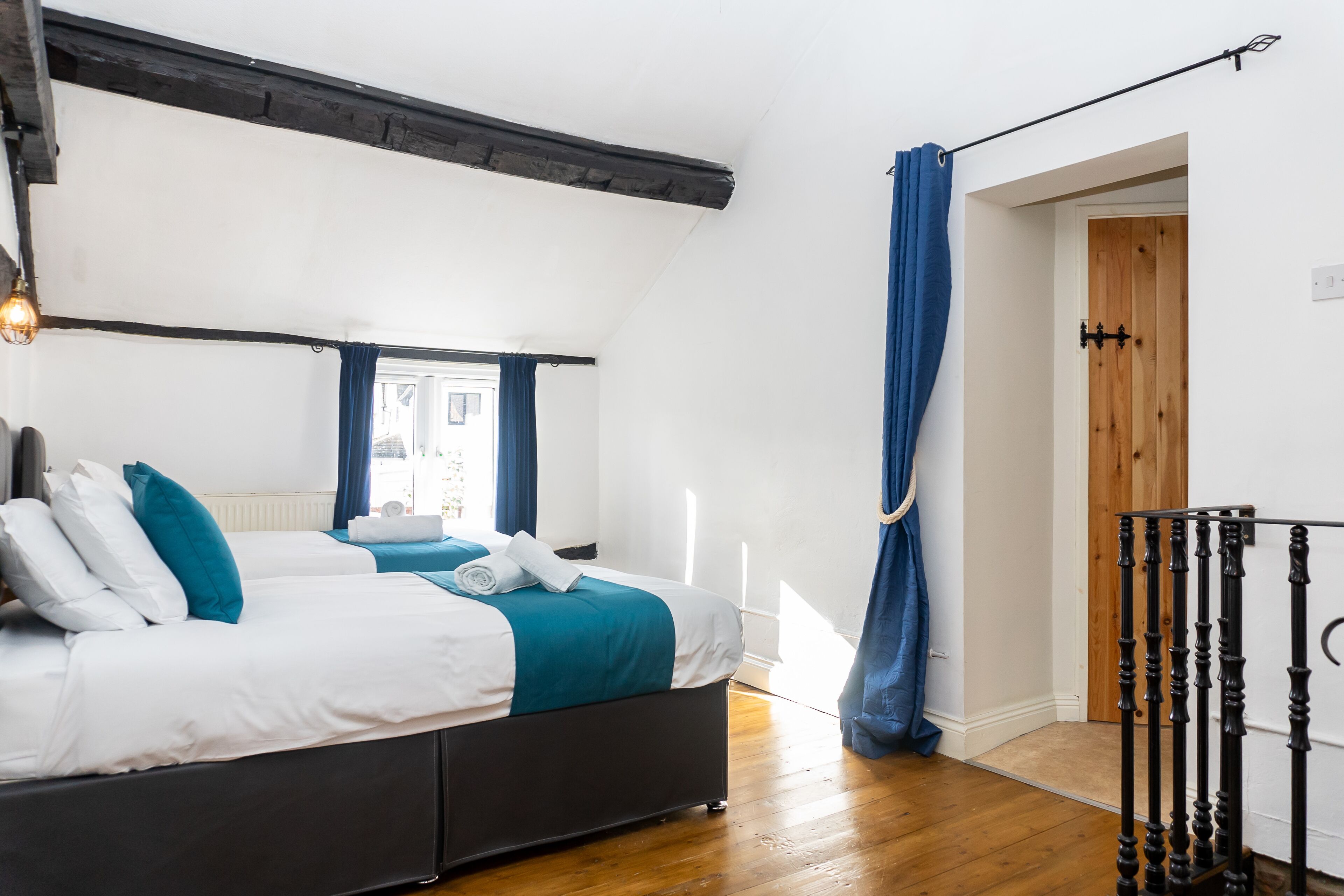 Une chambre à coucher avec un lit, une fenêtre avec des rideaux, un plancher en bois et une rambarde noire.