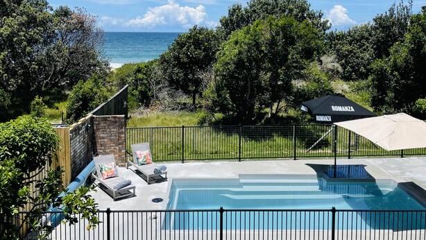 Una piscina amb vistes a l'oceà, envoltada per una tanca i vegetació.