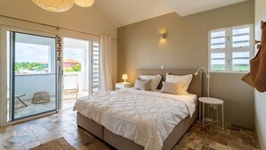 Et soveværelse med en stor seng, en skydedør til en balkon, et lille bord med en lampe og udsigt udad.