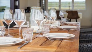 Una mesa de comedor dispuesta con copas de vino, platos y cubiertos, con vistas al exterior a través de amplios ventanales.