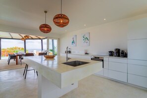 A modern kitchen with a central island, white cabinetry, and hanging wicker pendant lights. - Villa Gemini with Private Pool and Sea View (Kralendijk)