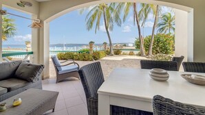 A covered outdoor seating area with wicker furniture, a white table, and a view of the sea and palm trees. - Port Bonaire Reef A601 with stunning sea views, a peaceful setting and everything on one level (Kralendijk)