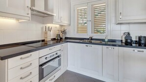 A modern kitchen with white cabinetry, a black countertop, and a window with blinds. - Port Bonaire Reef A601 with stunning sea views, a peaceful setting and everything on one level (Kralendijk)