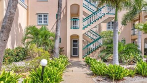 A multi-story building with a central staircase, surrounded by palm trees and various plants. - Port Bonaire Reef A601 with stunning sea views, a peaceful setting and everything on one level (Kralendijk)