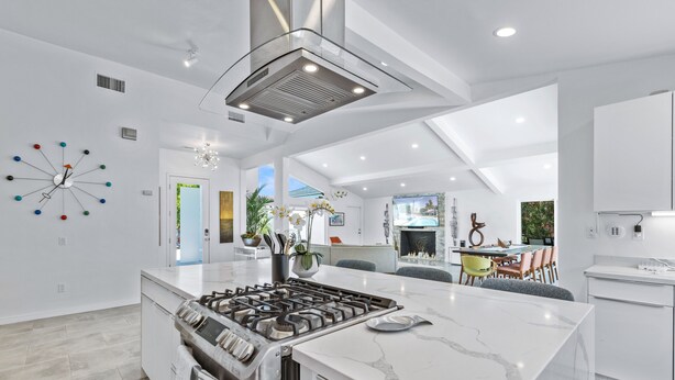 Une cuisine moderne dotée d’un îlot central, d’une cuisinière intégrée et d’un coin repas avec vue sur la piscine.
