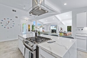 A modern kitchen with a central island, a built-in stove, and a dining area with a pool view. - Mid Century Cool - Rancho Mirage Home (Rancho Mirage)