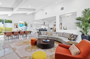 A spacious living area with a large sofa, a coffee table, and a dining table with chairs.