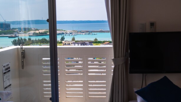 A balcony with a view of the sea and a TV mounted on the wall. - Crystal Court (Miyakojima)